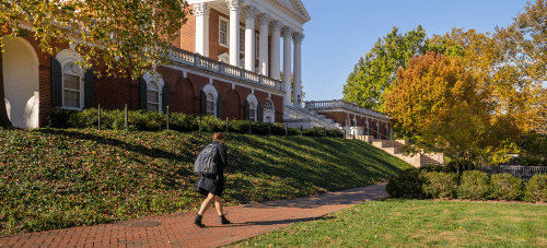 A student walking down a red brick path on the UVA grounds