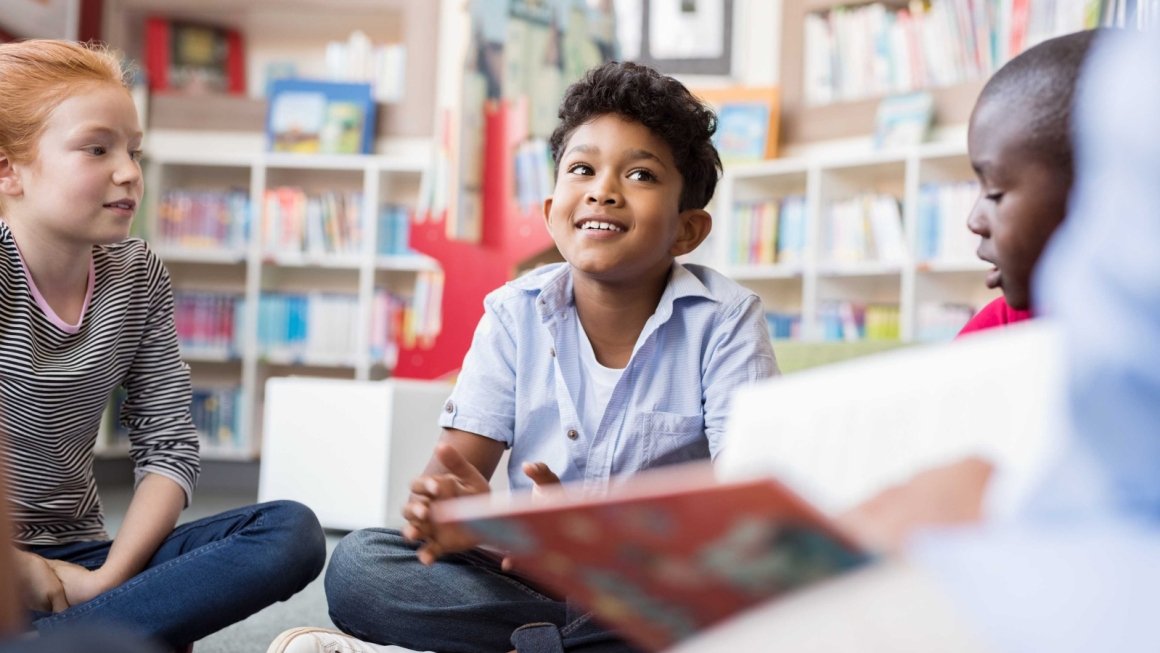 Elementary age children sit on the floor of a library in a circle