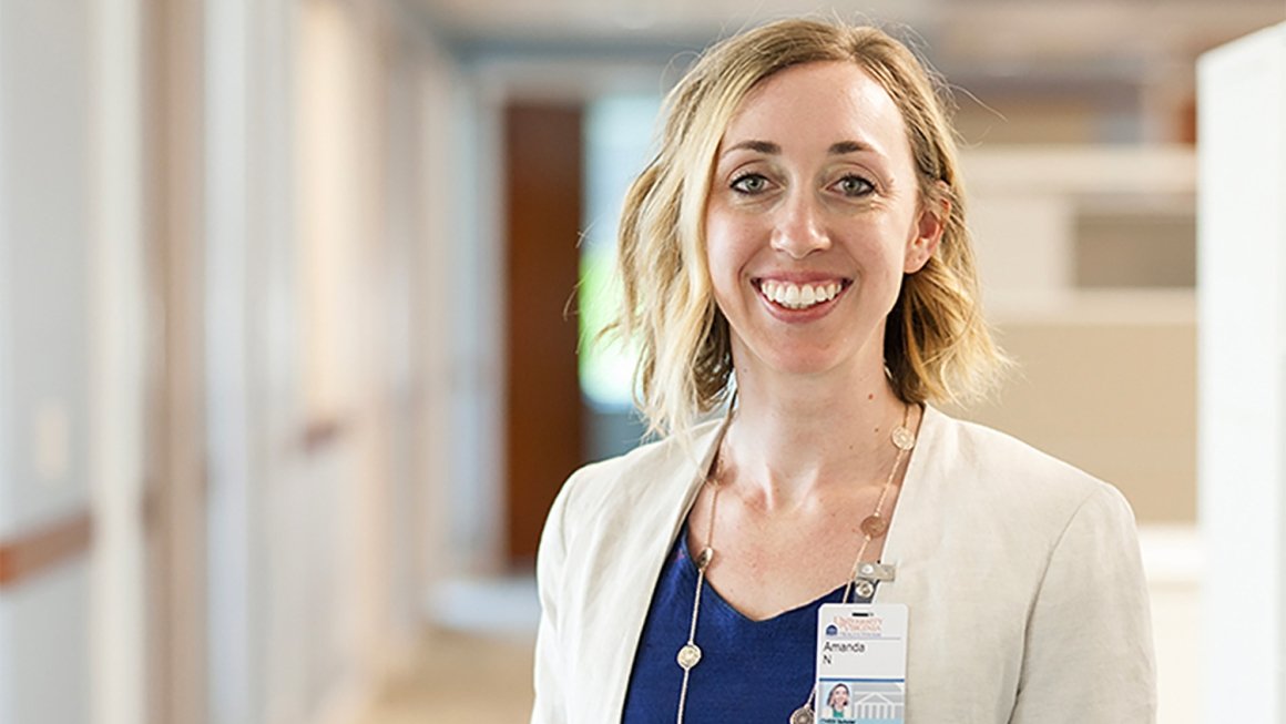 A woman with short blonde hair stands in a hospital hallway, smiling at the camera