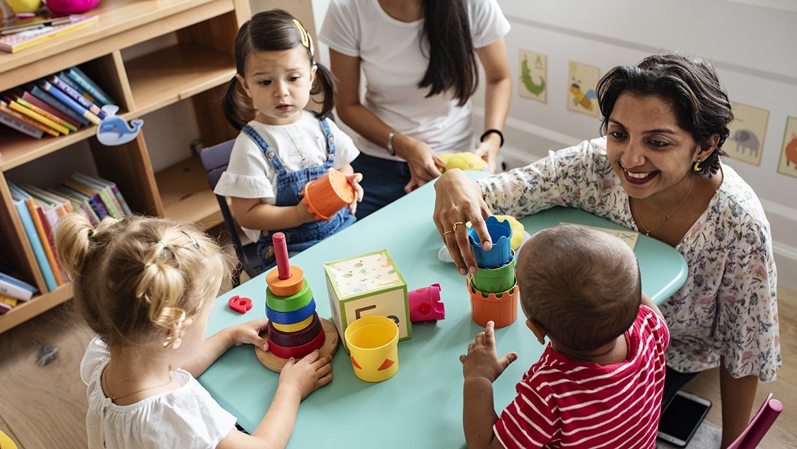 teacher plays with toys at a table with three young children