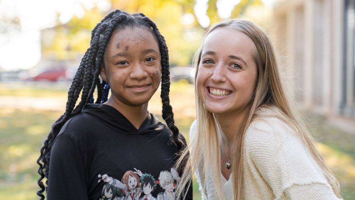 A college-age woman and a middle school girl smile at the camera