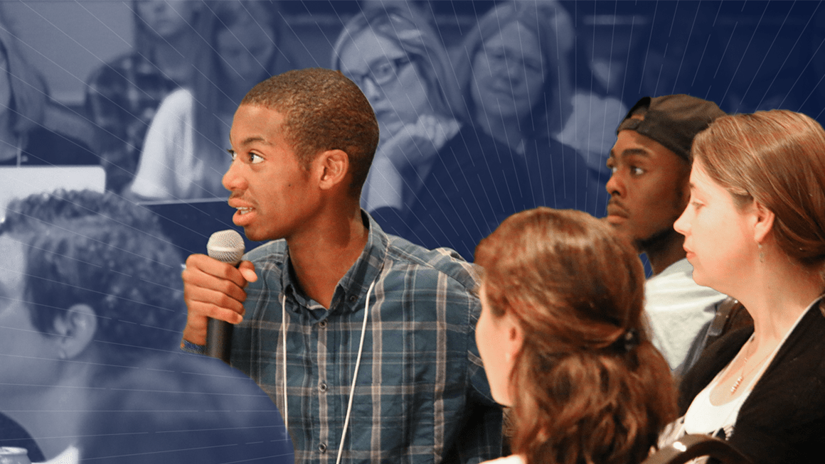 Youth speaks into microphone at table with other youth. 