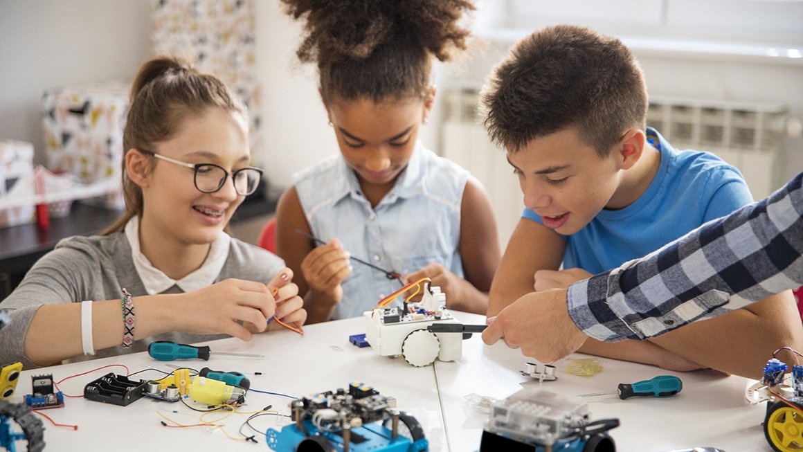 Three students at table playing with robotics parts