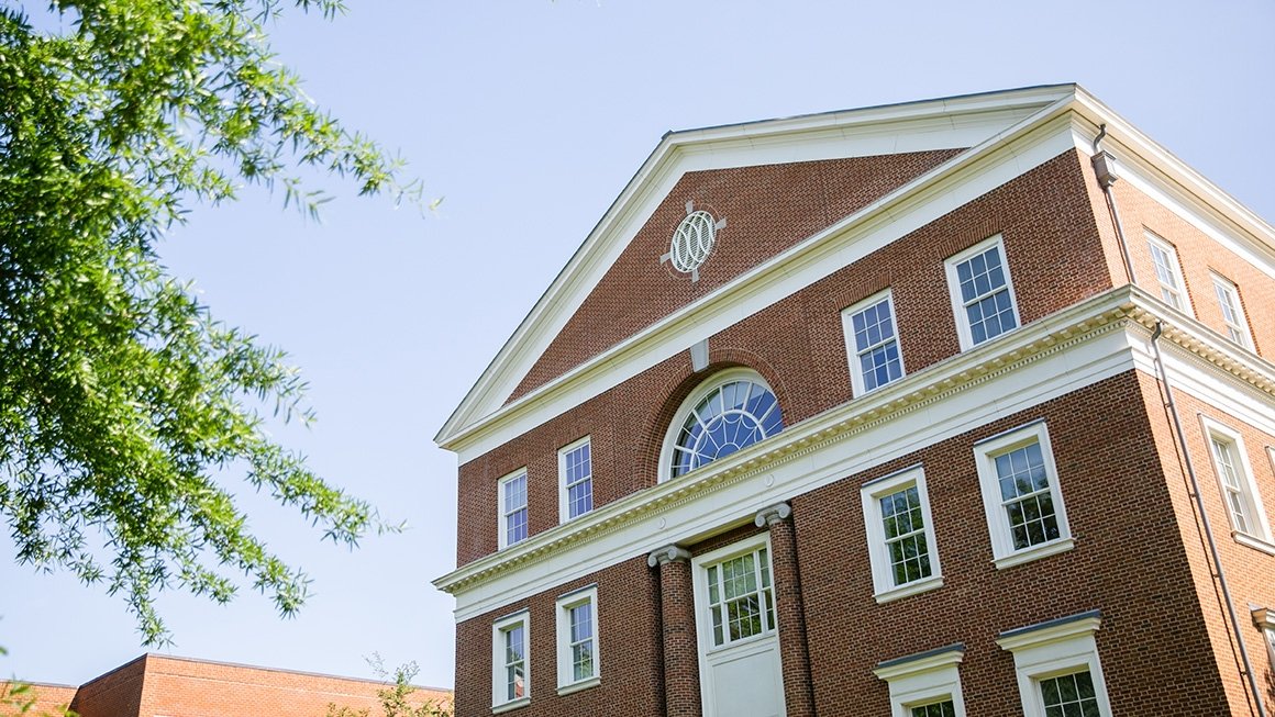 Bavaro Hall, a brick building with white trim, surrounded by a blue sky and green trees