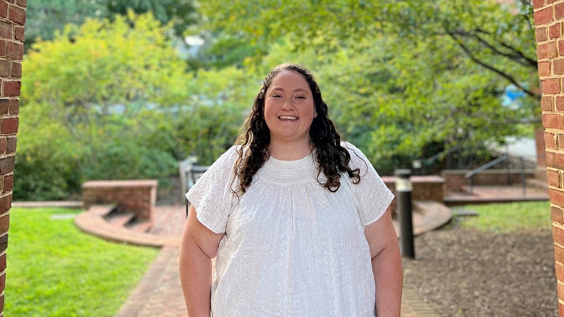 Danielle Hutcherson, wearing a white top, stands outside under a brick archway and smiling