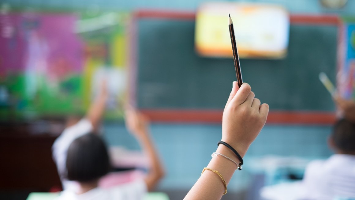 Student's hand raised in class holding a pencil 