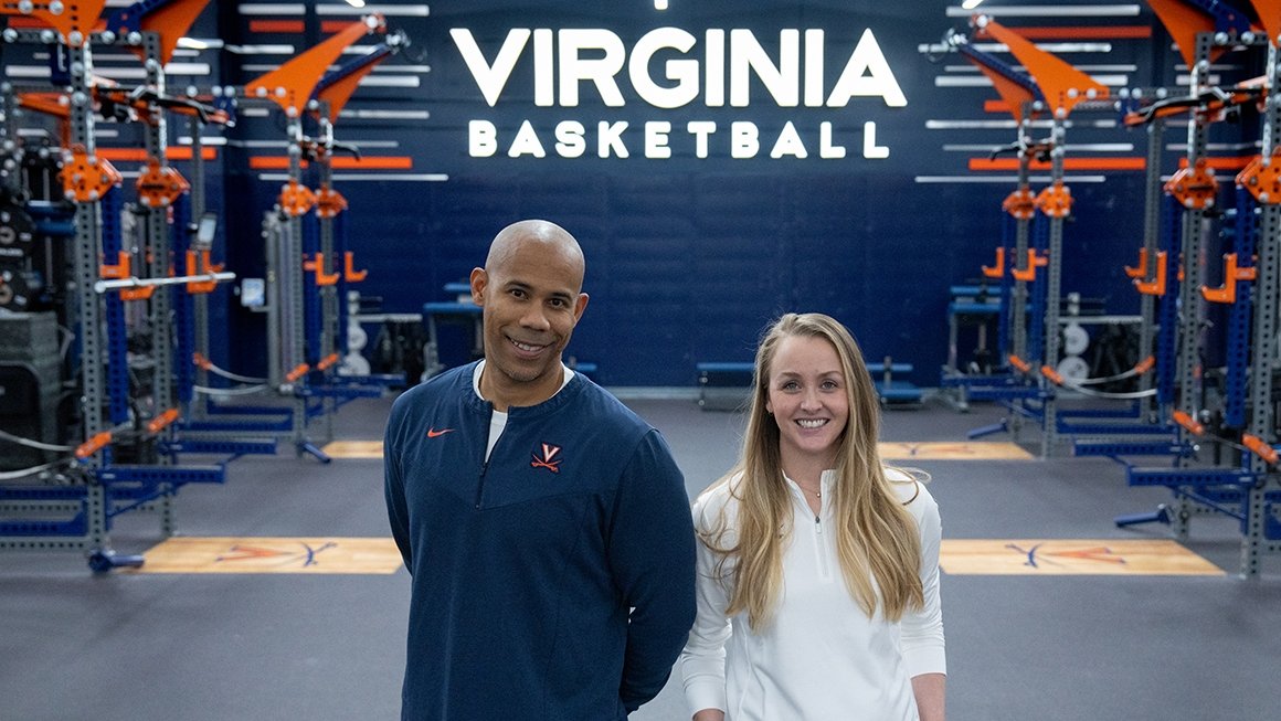 Mike Curtis and Natalie Kupperman standing in the middle of the weight room looking at the camera, smiling