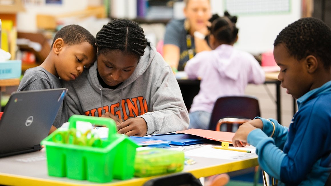 Young boy leans close to his teacher as they both examine something on the child's desk