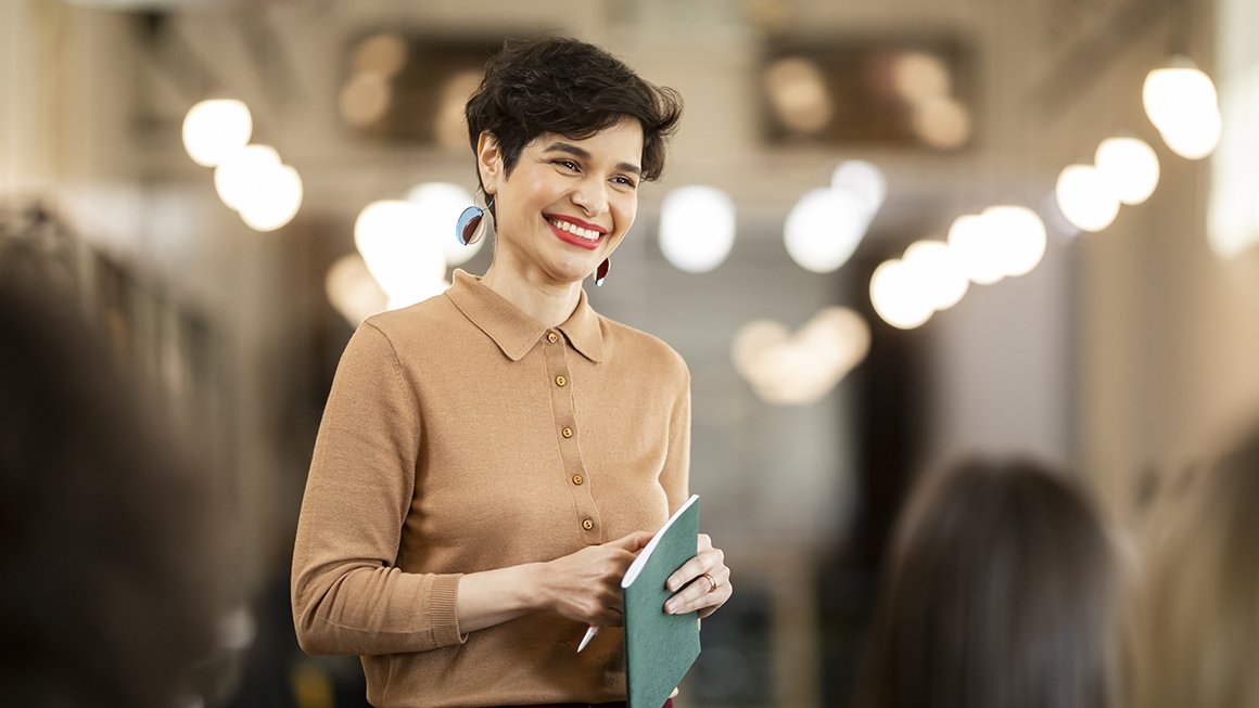 Woman stands, smiling, holding a pen and a folder in her hands