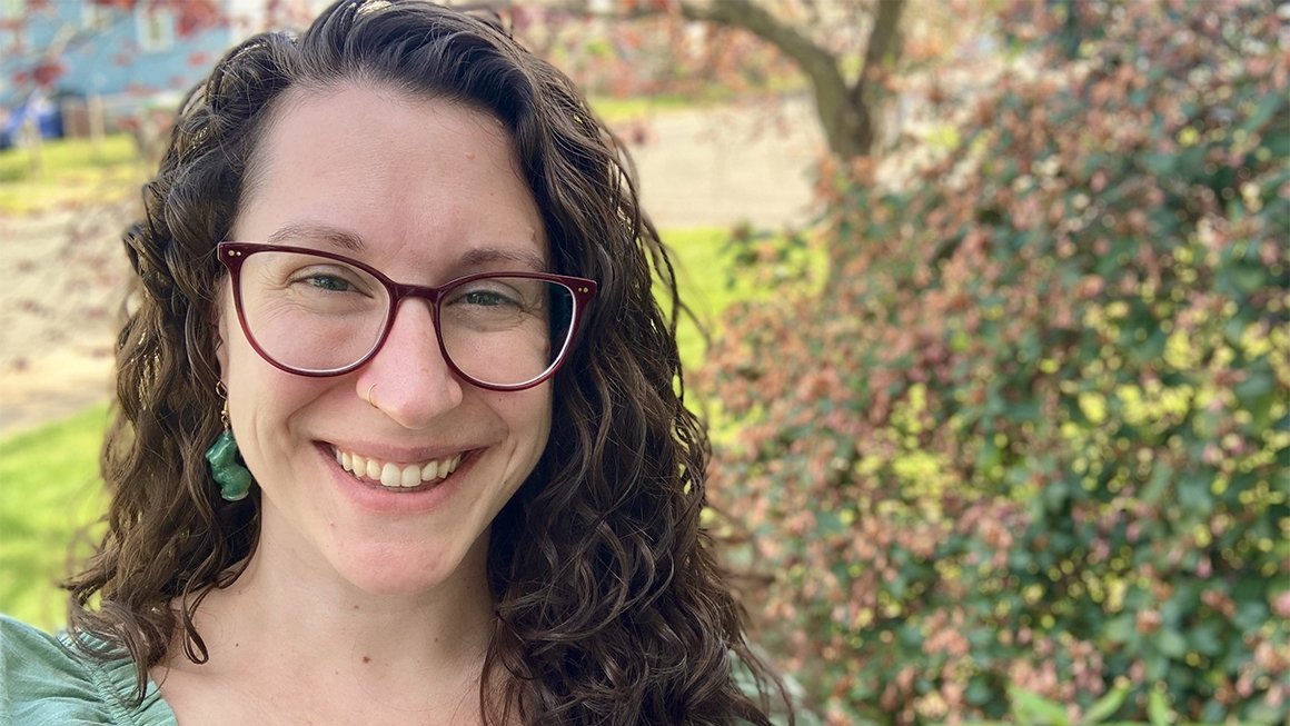 Theresa Pfister smiles at the camera against a backdrop of green leaves