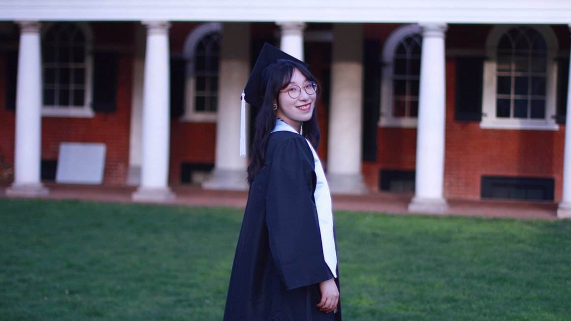 Polly Wu stands on the lawn wearing her graduation cap and gown