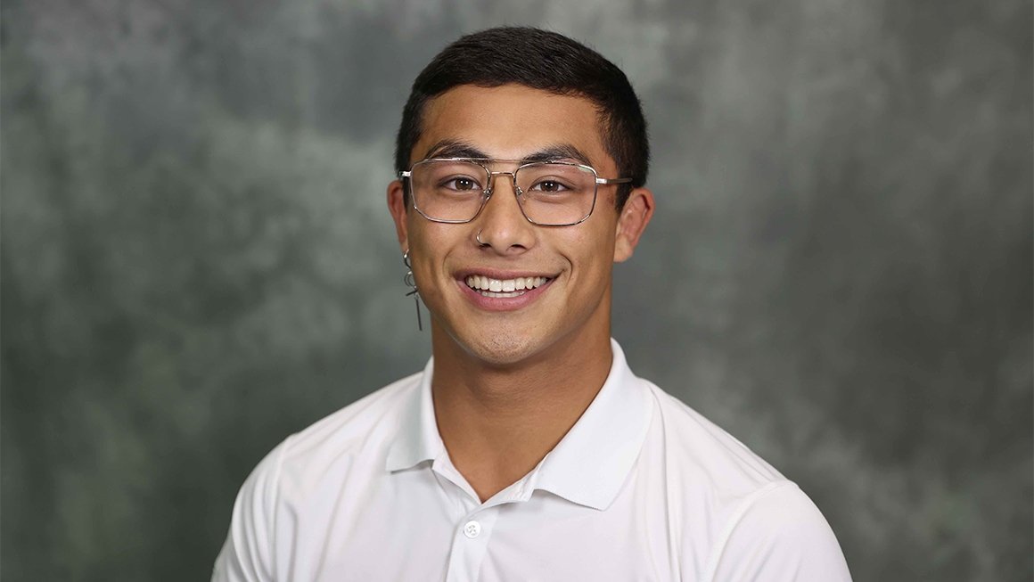 Alexander Cruz wearing glasses and a white collared shirt against a gray backdrop