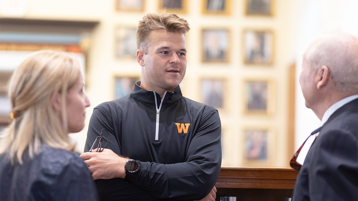 Jackson Matteo, wearing a dark zip-up pullover, smiling and talking with two other people