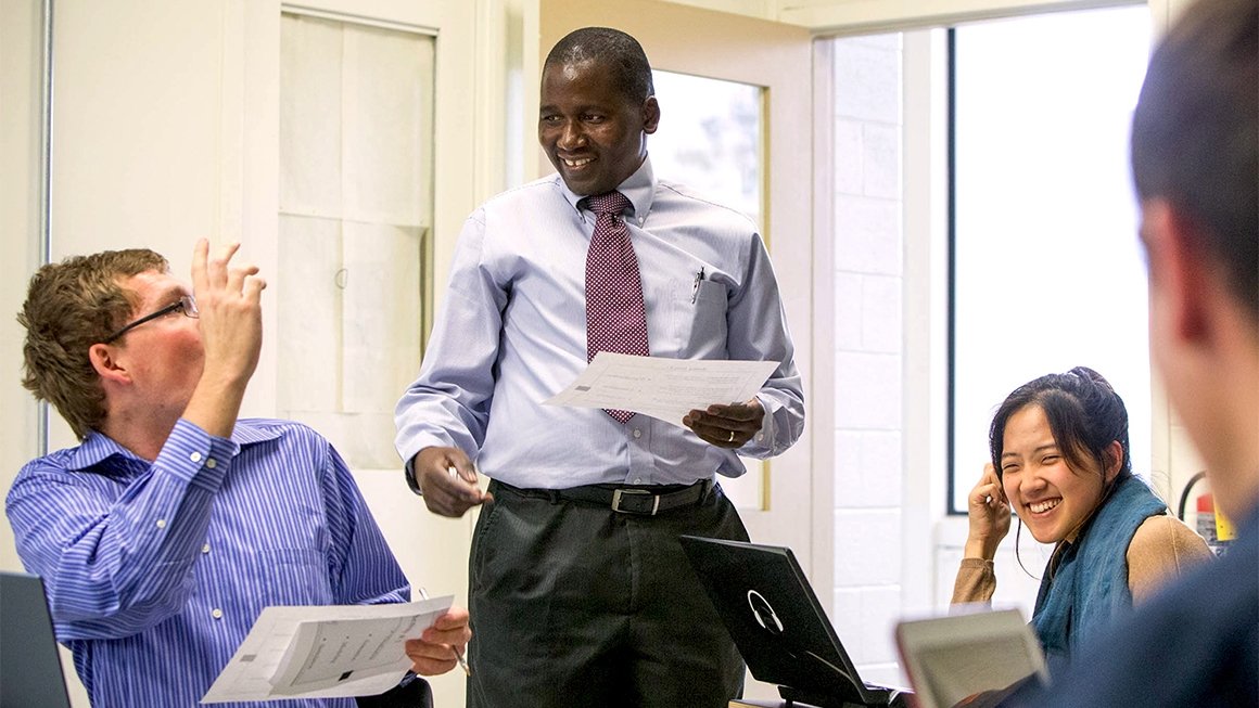 Frackson Mumba, wearing a collared shirt and tie, laughs and converses with a student