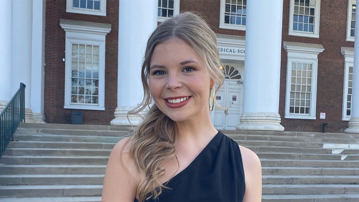 Kennedy Wilkins stands in front of the steps and white columns of the UVA Rotunda, wearing a black dress and smiling at the camera
