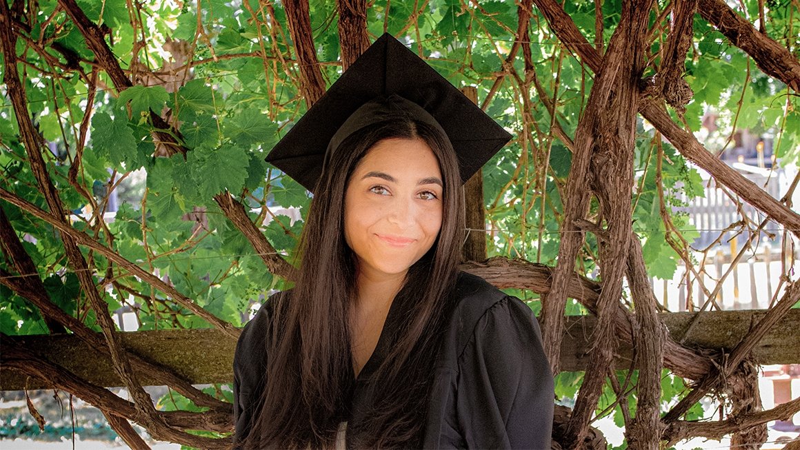 Paria Harirsaz wearing a graduation cap and gown standing in front of a tree