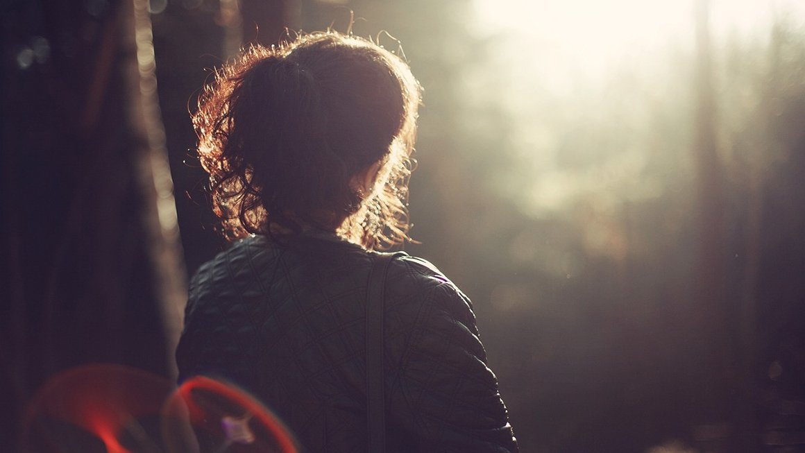 Back of woman's head as she stares into nature toward sunshine