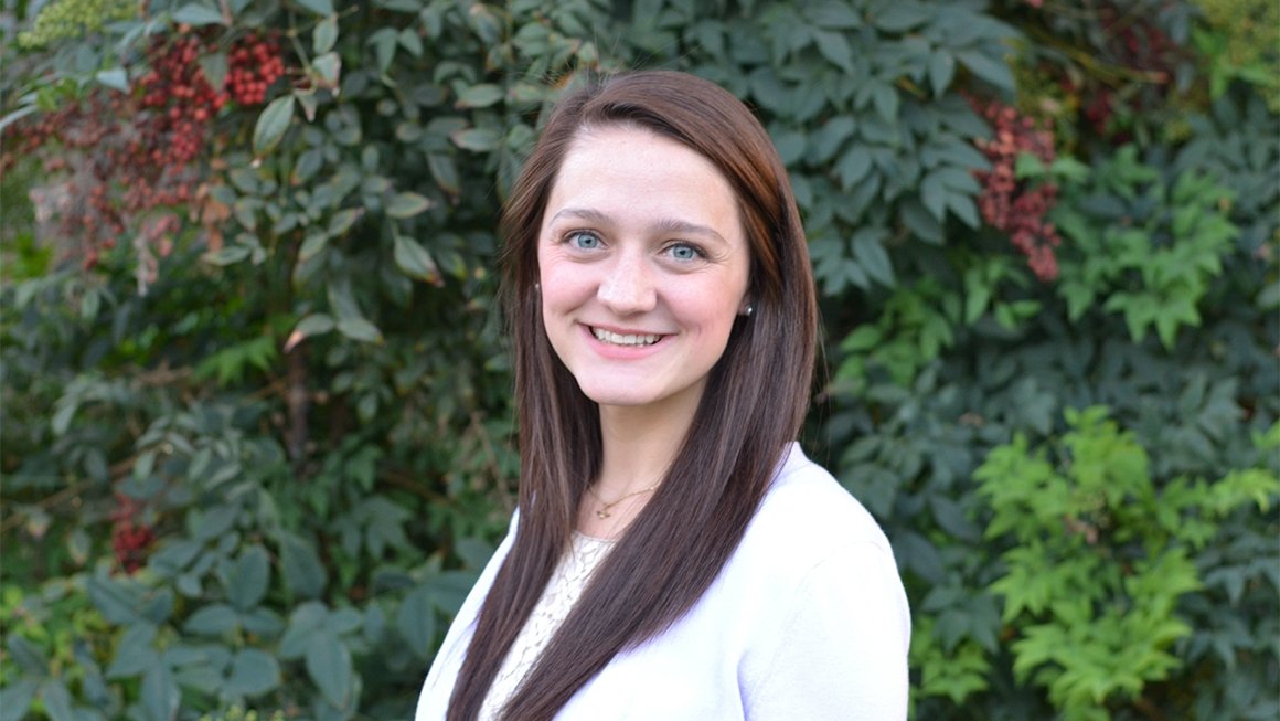 Elizabeth Carr smiles at the camera against a backdrop of green leaves