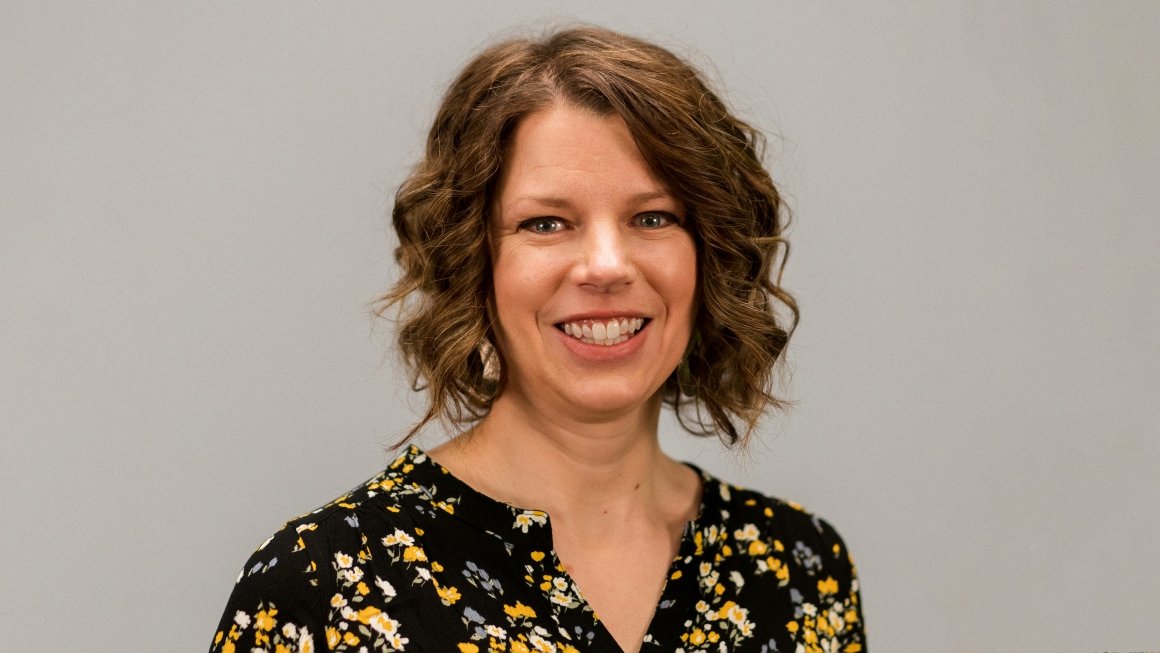 Headshot of Kristina Fulton wearing a black and yellow top against a gray background