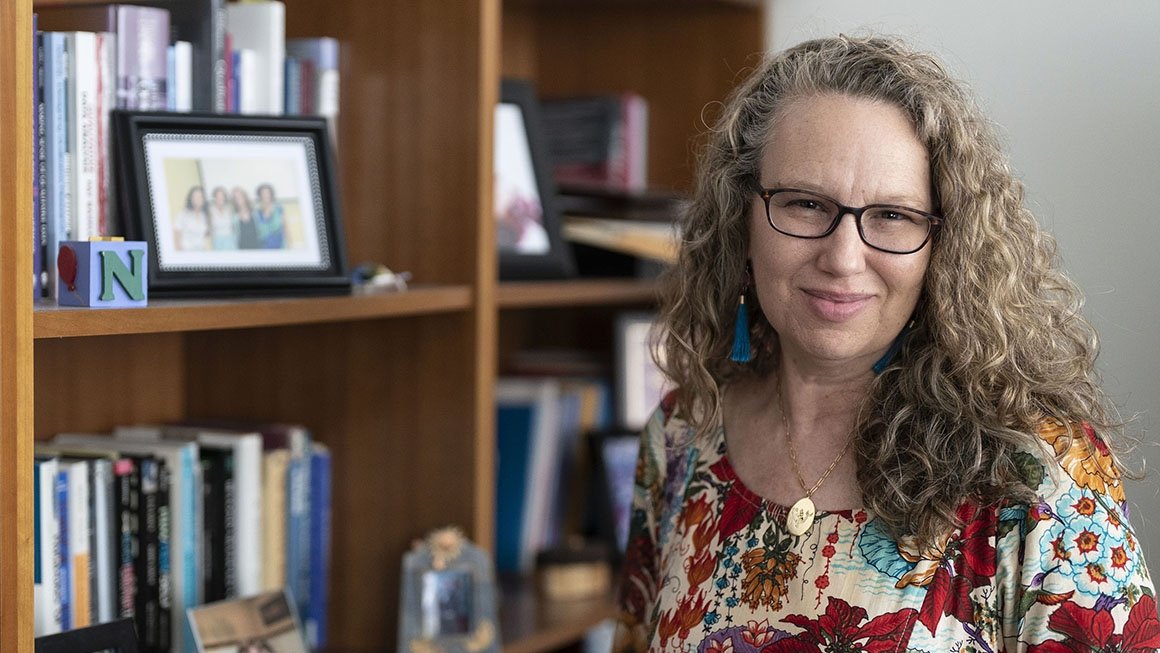 Nancy Deutsch stands in front of a bookshelf with books and framed phots in her office