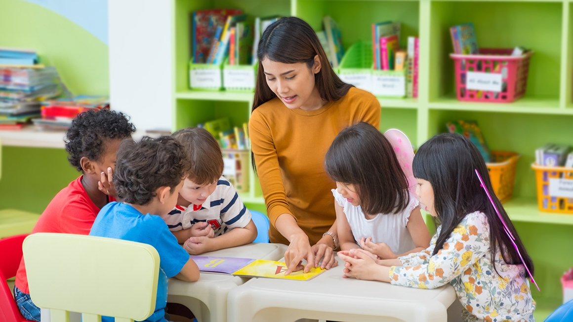 Teacher sits at small table with 5 young students