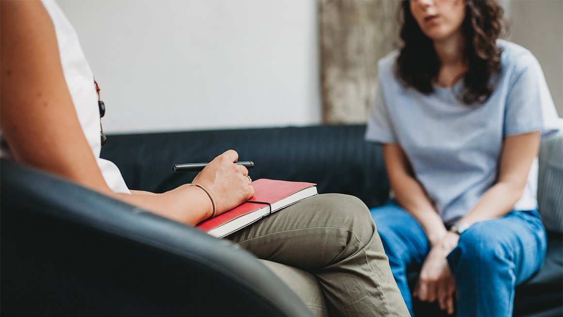 Someone holding a notebook and pen talks with a young person who looks upset