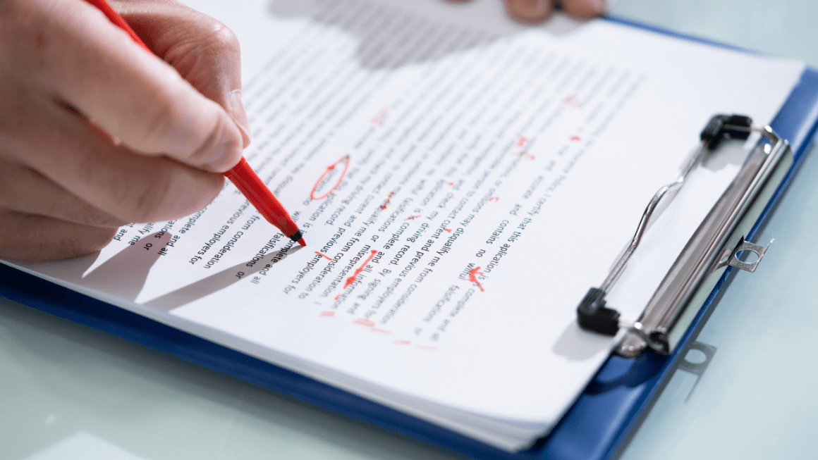 A printed essay on a clipboard being marked up by someone using a red pen