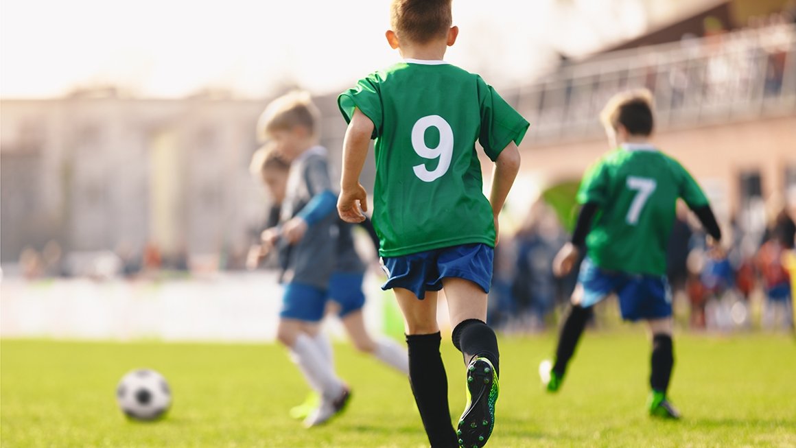 Boy in green jersey with no. 9 on it runs after soccer ball. Four other boys are in the background