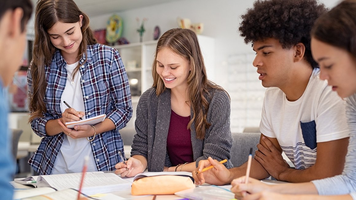 Teens work together on a project, sitting at a table.