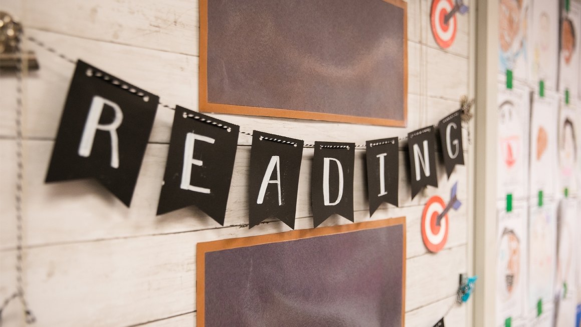 A black and white banner hanging on an elementary classroom wall says "Reading"