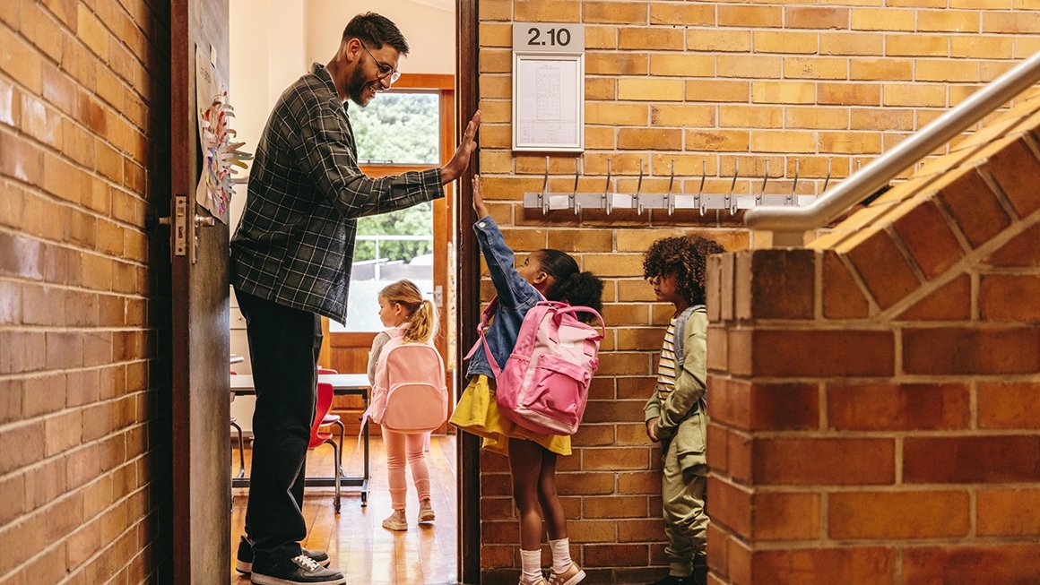 Male teacher high fives young student as she enters a classroom.