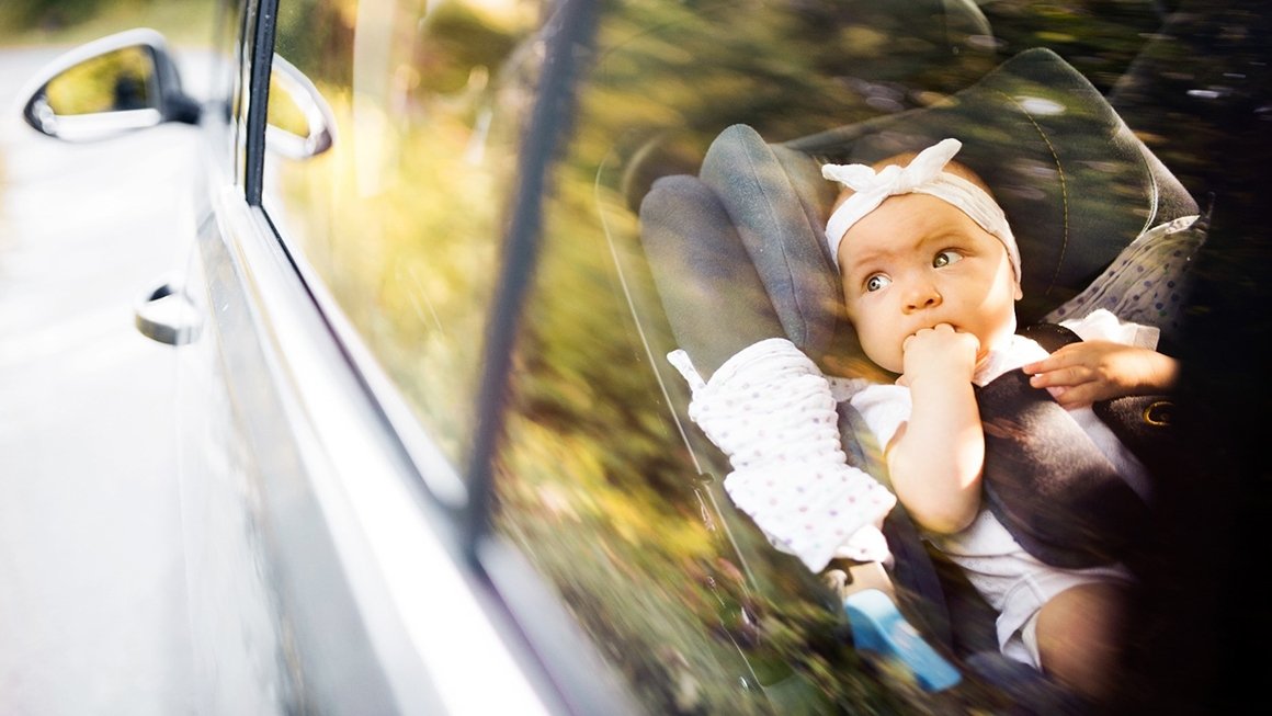 Baby in a carseat looks out the window of the back seat of a car.