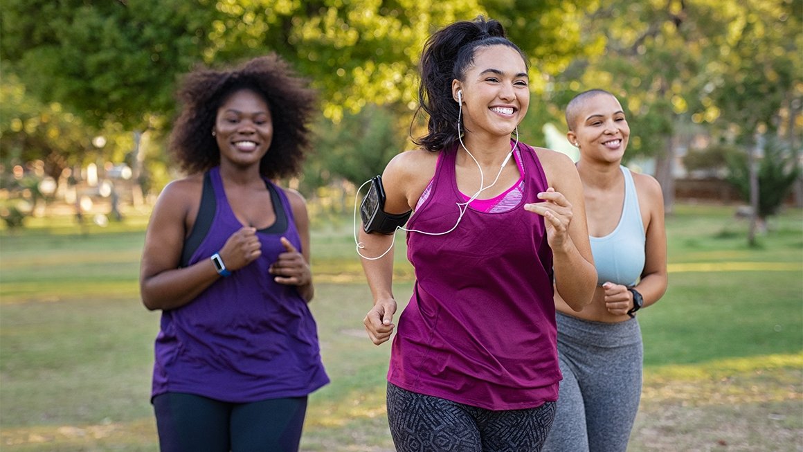 Three women smile while jogging through a park together
