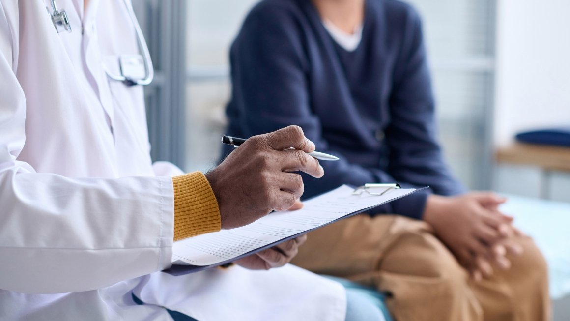 A physician sits next to a young adult patient.