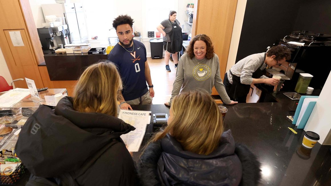 Two employees at Kindness Cafe take orders from two customers at the counter. Two employees make coffees in the background.