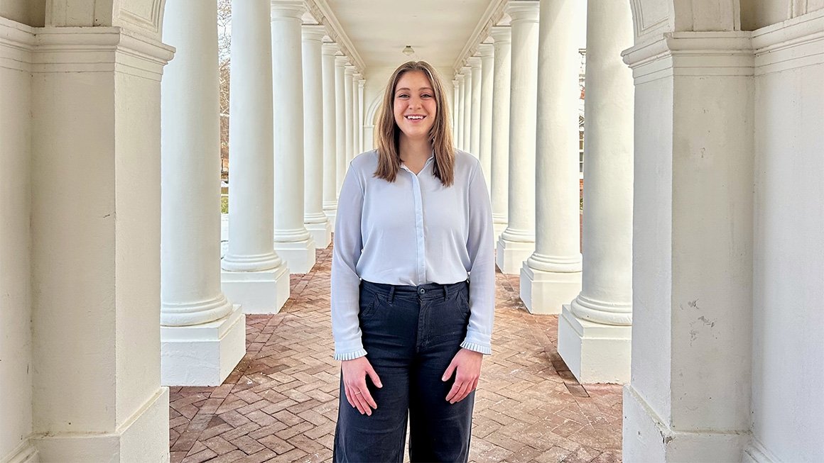 Natalie Behnke stands outside smiling surrounded by white columns