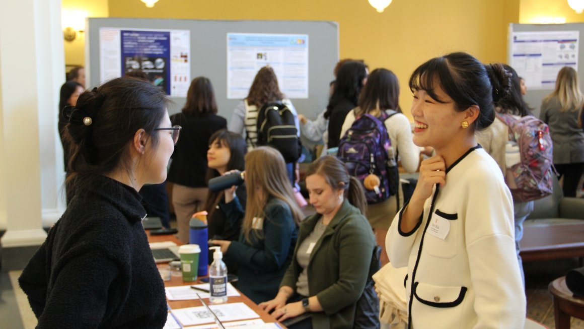 Two people smiling and talking in front of a research poster session