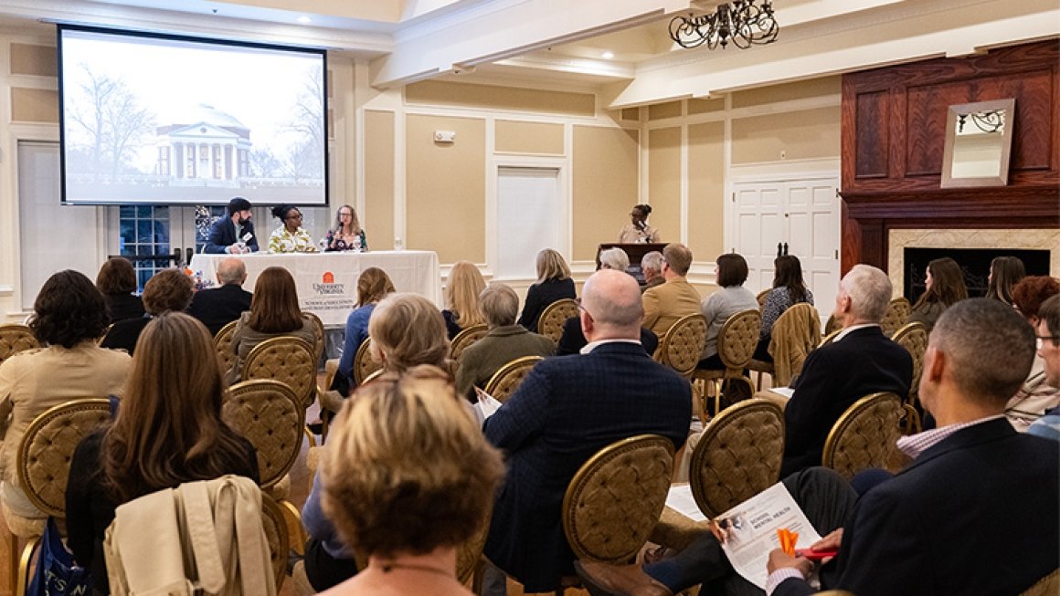 Three panelists sitting at a table and a moderator at a podium speak to a room full of people