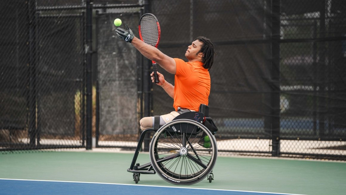Brian Douglas serves a tennis ball sitting in a wheelchair