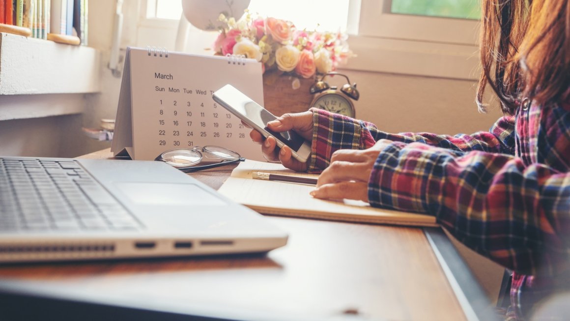 Teen uses phone and laptop sitting at desk in their room