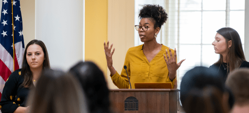 A graduate student speaking at a podium in front of a group of people