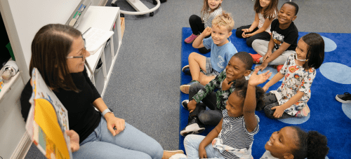 An educator in a classroom reading a book to a group of children sitting on the floor