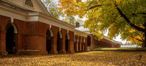 A red brick building with a covered walkway to the left with fall foliage to the right