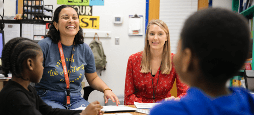 Two teachers working with students at a table in a classroom.