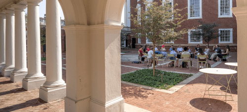 An exterior shot of a courtyard between two UVA buildings with students sitting in a circle having class