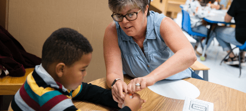 A teacher and a child working together at a classroom table