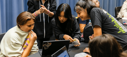 A group of students and a teacher working together around a laptop