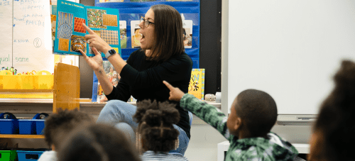 A teacher at the front of a classroom reading a book to students