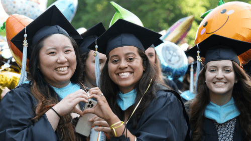 Smiling students wearing graduation robes and surrounding by balloons