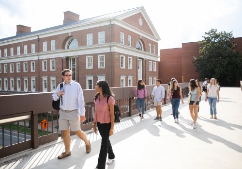 Students walk across the pedestrian bridge with Bavaro Hall in the background
